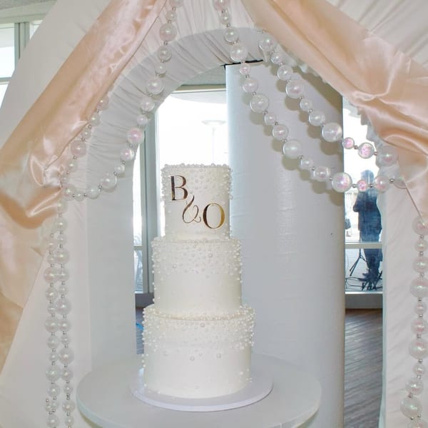 Pearl wedding cake with B&O monogram under draped archway