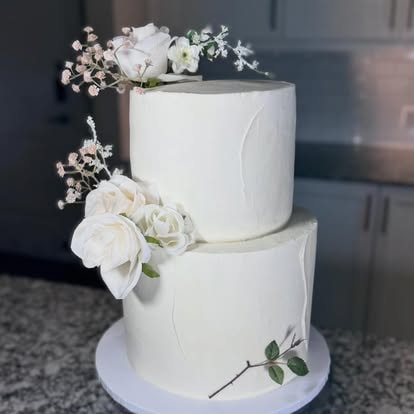 Two tier white wedding cake with fresh white roses and baby breath