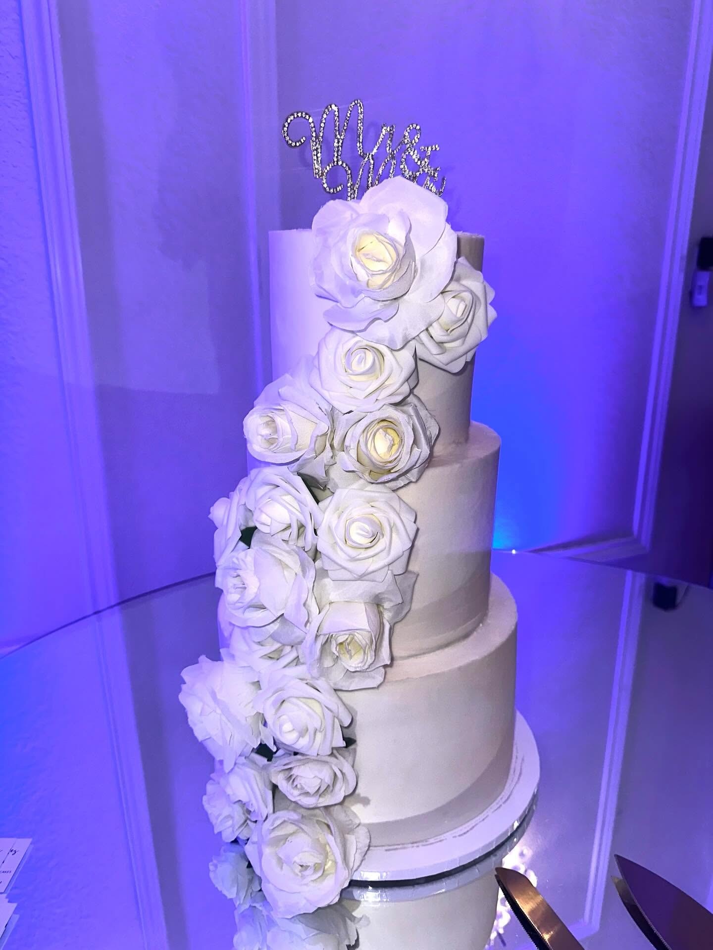 Four tier white wedding cake with cascading white roses and rhinestone topper